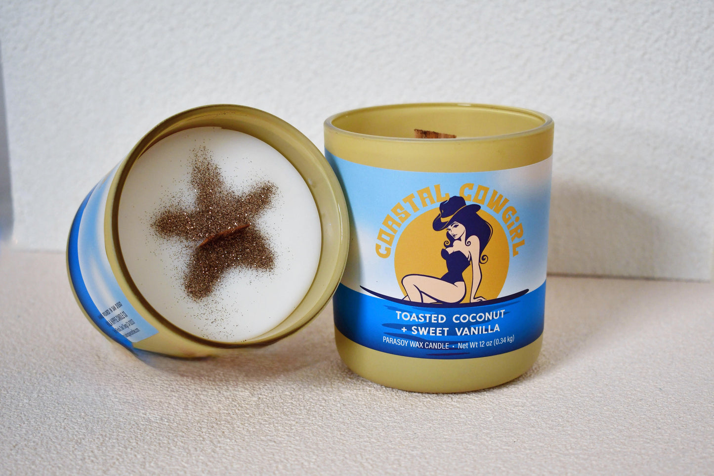Two 12 oz toasted coconut and sweet vanilla scented candles with wooden wicks and starfish glitter design on the soy wax surface. Ideal for beach-themed decor or gifts.