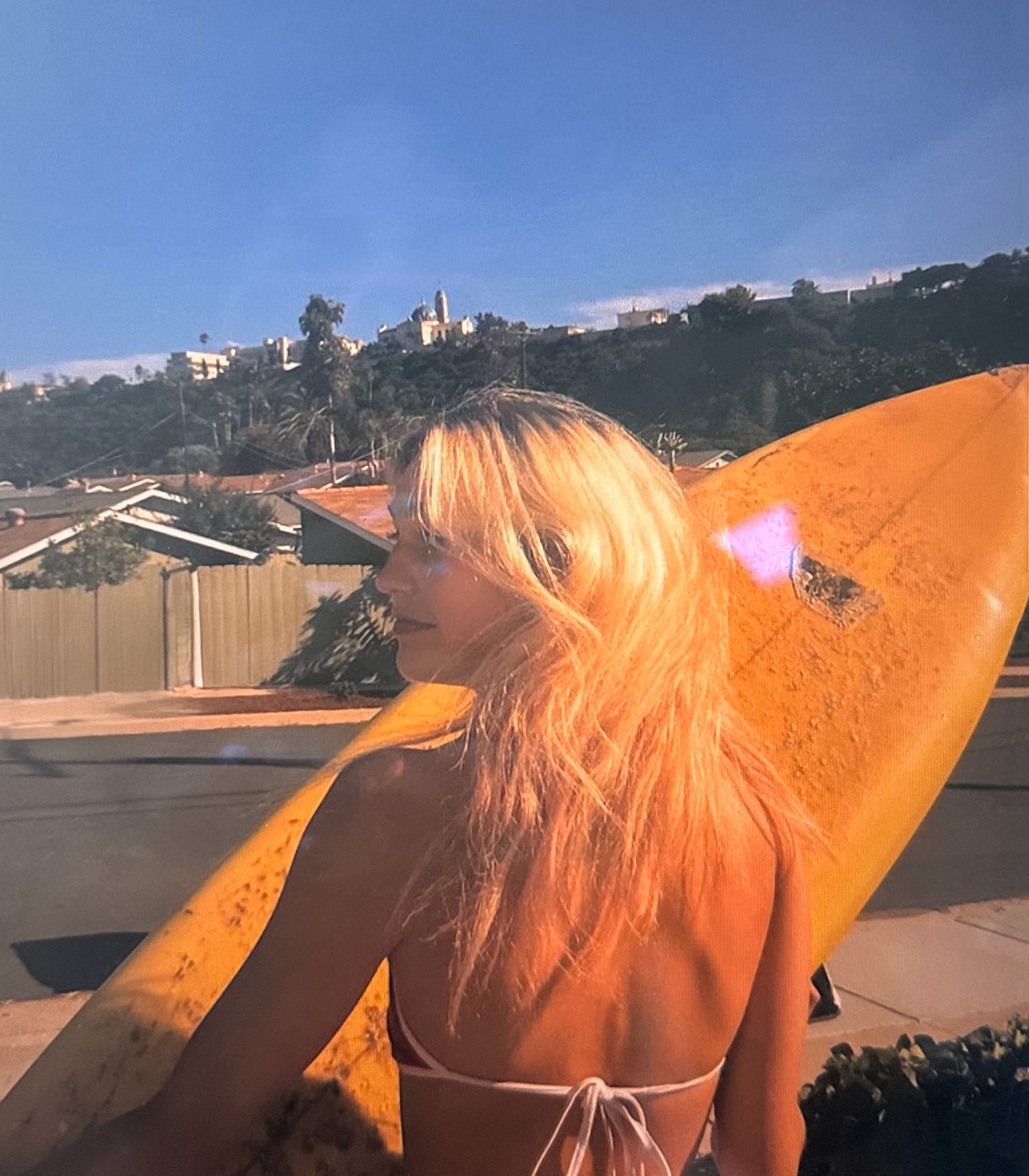 Farren Simon, owner, looking over her shoulder holding a surf board on a sunny day.