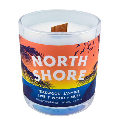 Right-side view of a scented candle in an iridescent jar labeled "North Shore" with notes of teakwood and jasmine.
