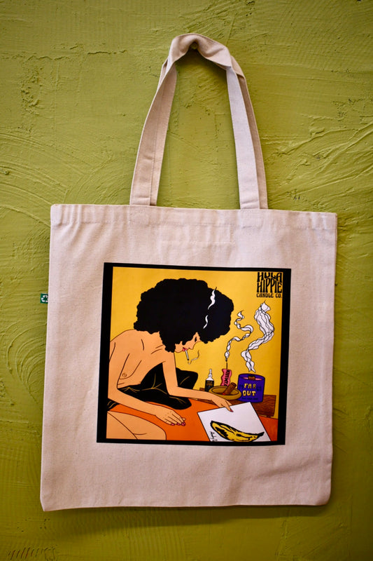 Hanging Canvas cream tote bag with image of a chill afro-woman smoking in bed and admiring the velvet underground recorded on a yellow background with candles burning behind and a small Hula Hippie Logo in the corner