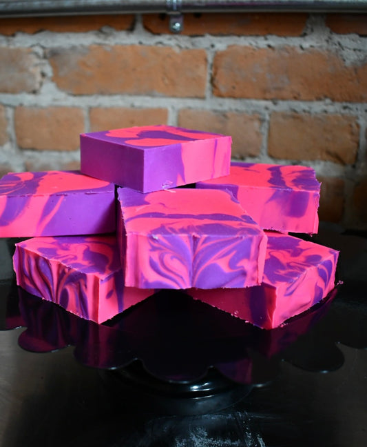 Stack of pink and purple marbled soap bars on a black stand against a brick wall.